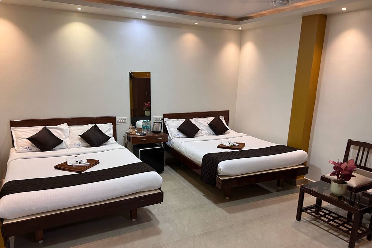 A hotel room with two beds, a small table with a chair, and a mirror on the wall.