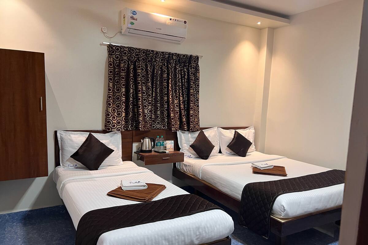 A hotel room with two beds, a wardrobe, an air conditioning unit, and a window with patterned curtains.