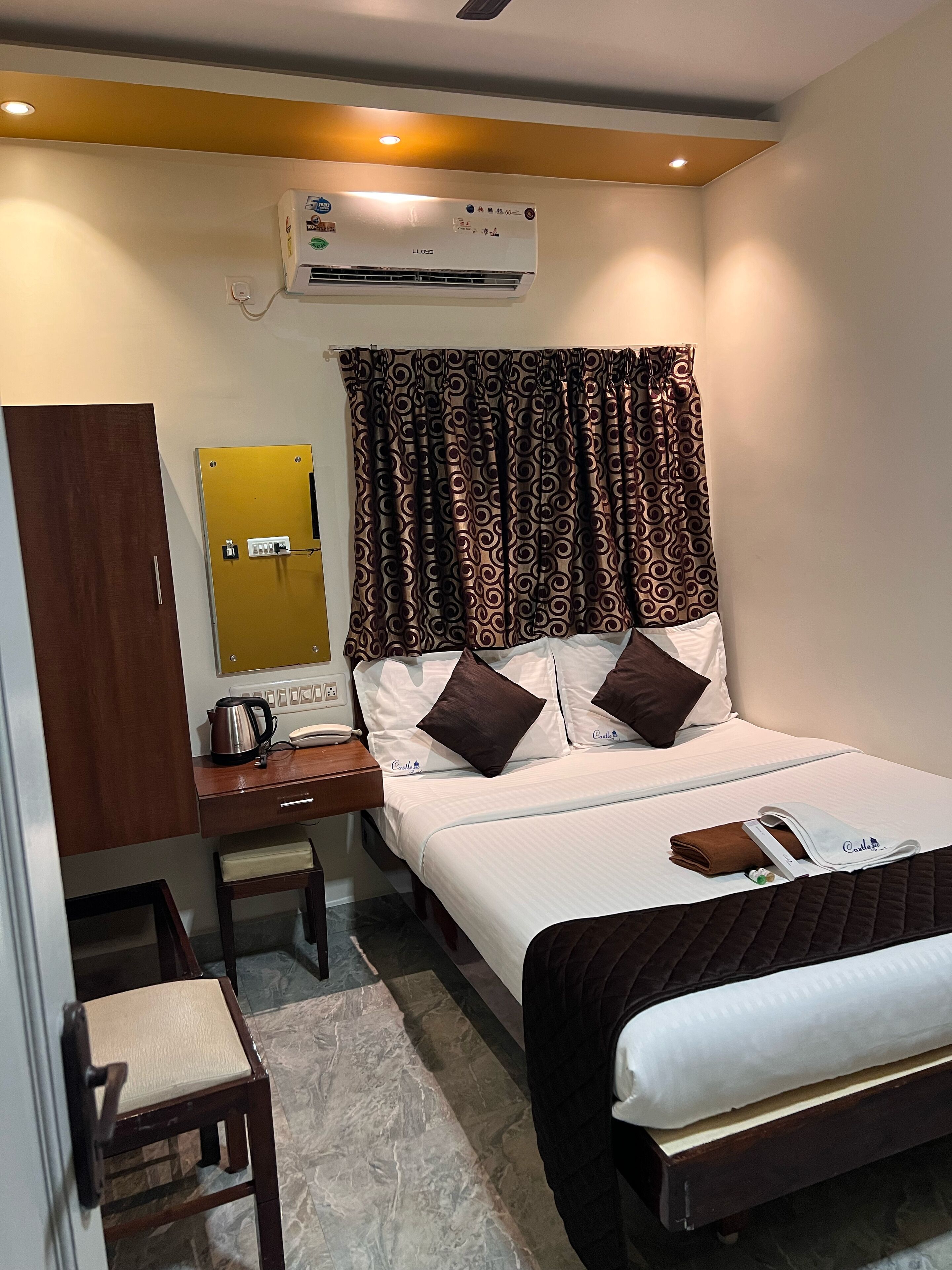 A hotel room with a bed, a desk, a chair, an air conditioning unit, and a telephone.
