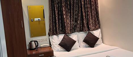A hotel room with a bed, a desk, a chair, an air conditioning unit, and a telephone.