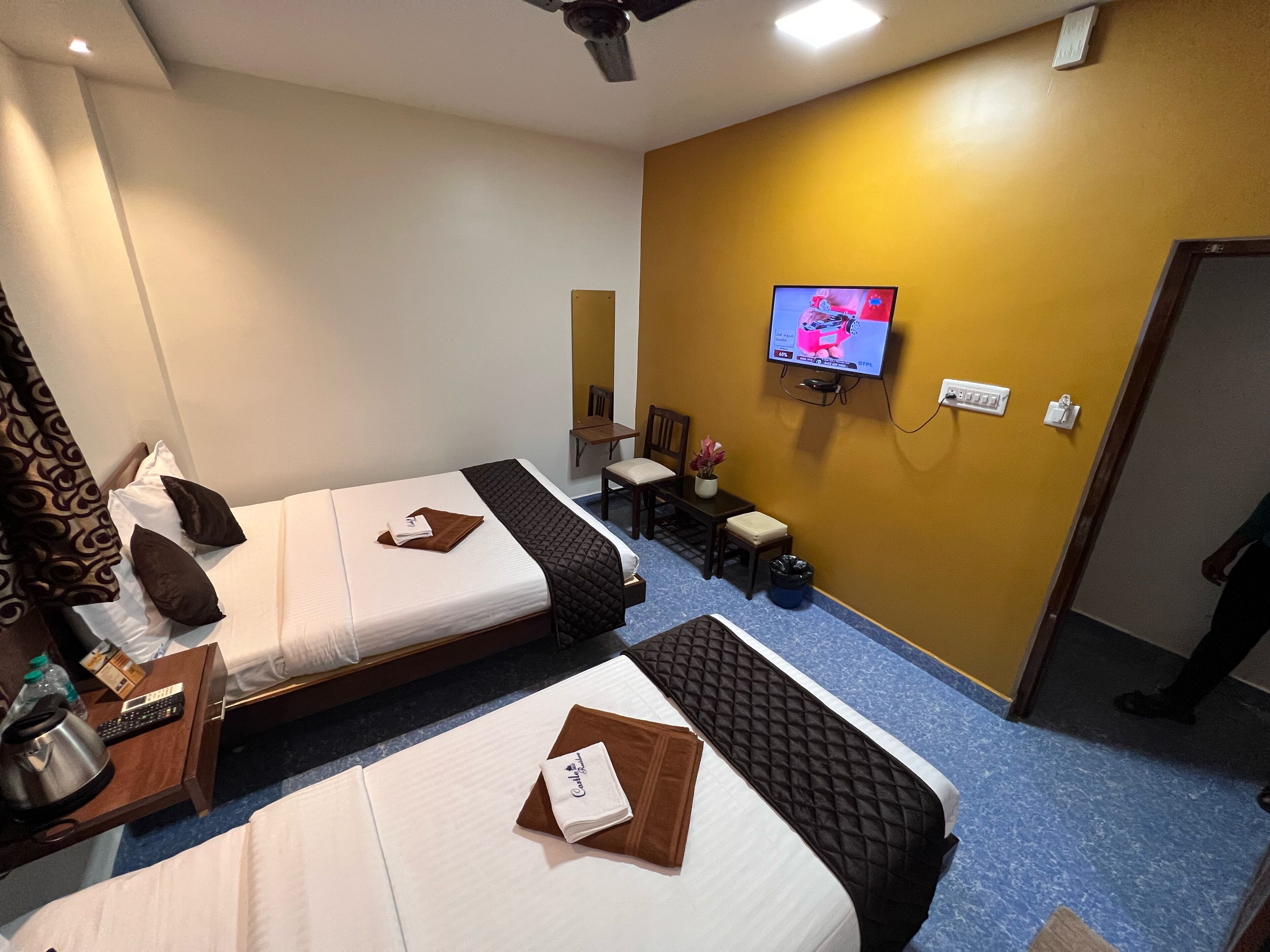 A hotel room with two beds, a TV on the wall, a small table with a chair, and a desk with a chair.