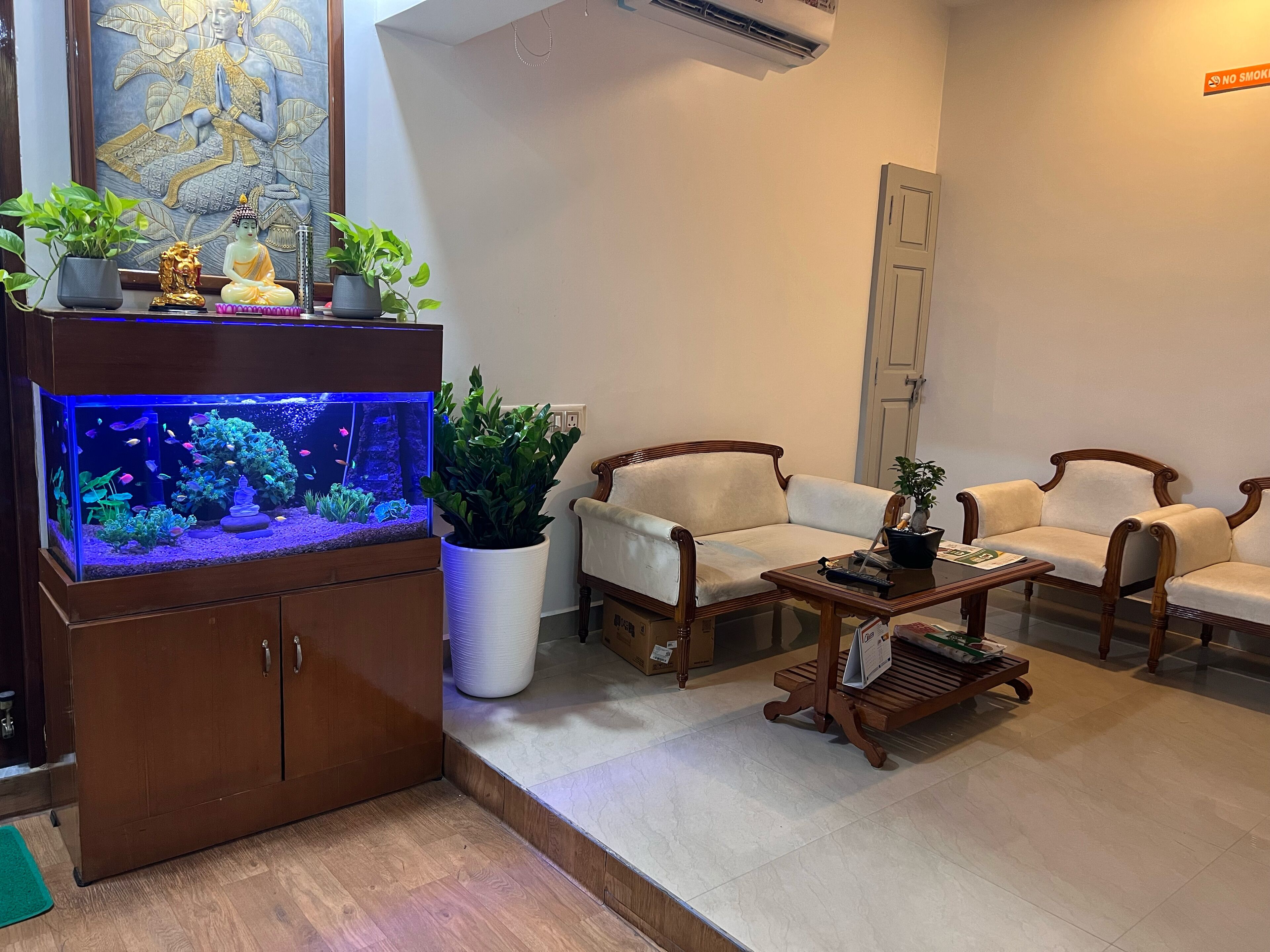 A living room with a large aquarium, two white sofas, a wooden coffee table, and a potted plant.