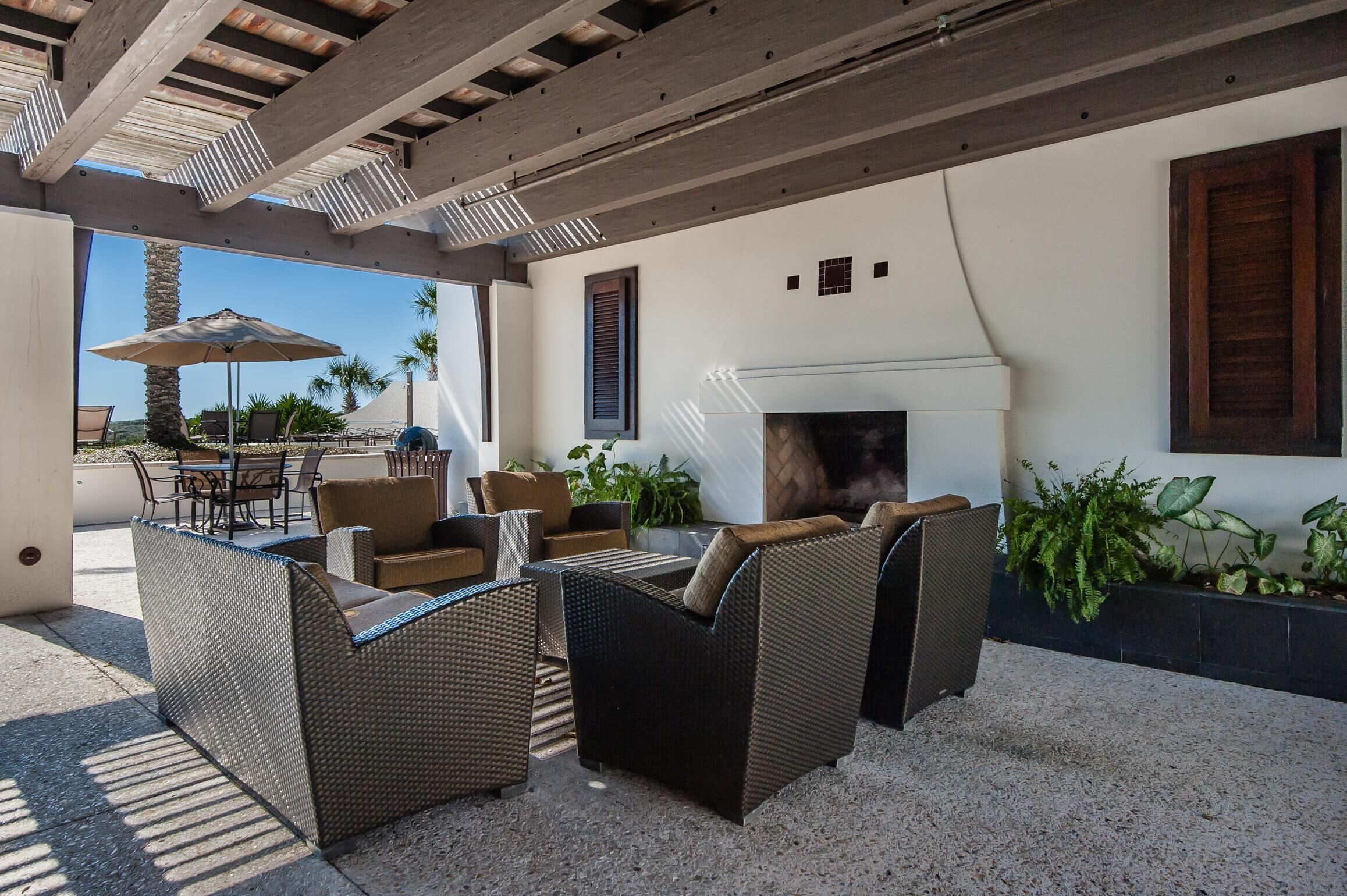 An outdoor patio area with wicker furniture, a white fireplace, and a view of palm trees.