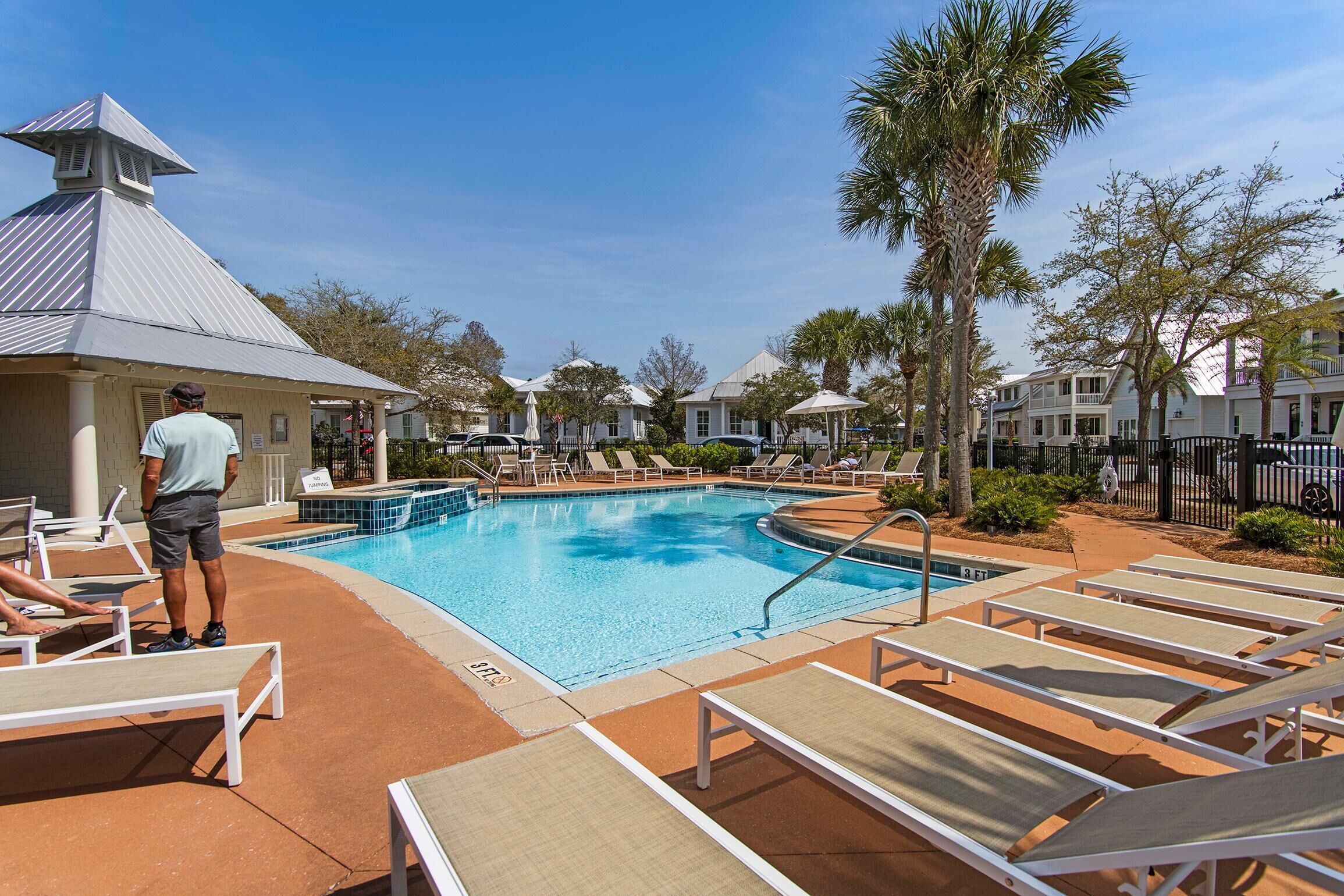 A swimming pool with lounge chairs, a lifeguard, and a building with a distinctive roof.