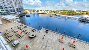 A waterfront deck with wooden benches and umbrellas, a dock, and a large building in the background. - Laketown Wharf 317 (Panama City Beach)