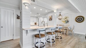 A kitchen with a white island, bar stools, a dining table, and chairs.