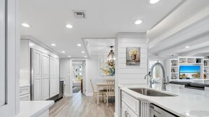 A modern kitchen with white cabinetry, a central island with a sink, and a dining area with a table and chairs.