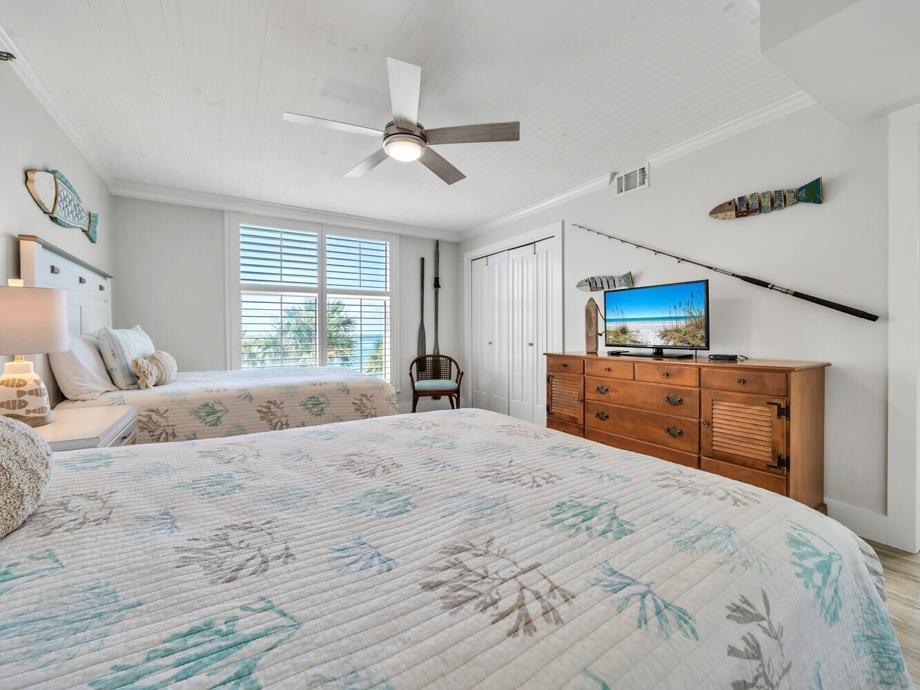 A bedroom with a large bed, a ceiling fan, a dresser, and a TV on a stand.