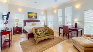 Une chambre spacieuse avec un grand lit, un coin salon avec un fauteuil, un bureau et un ventilateur de plafond.