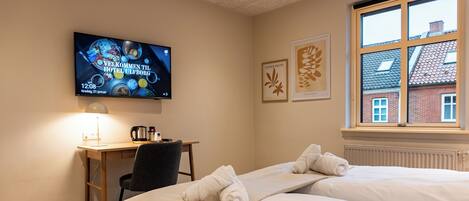A hotel room with a bed, a desk, a chair, a TV displaying a welcome message, and a window with a view of a house.