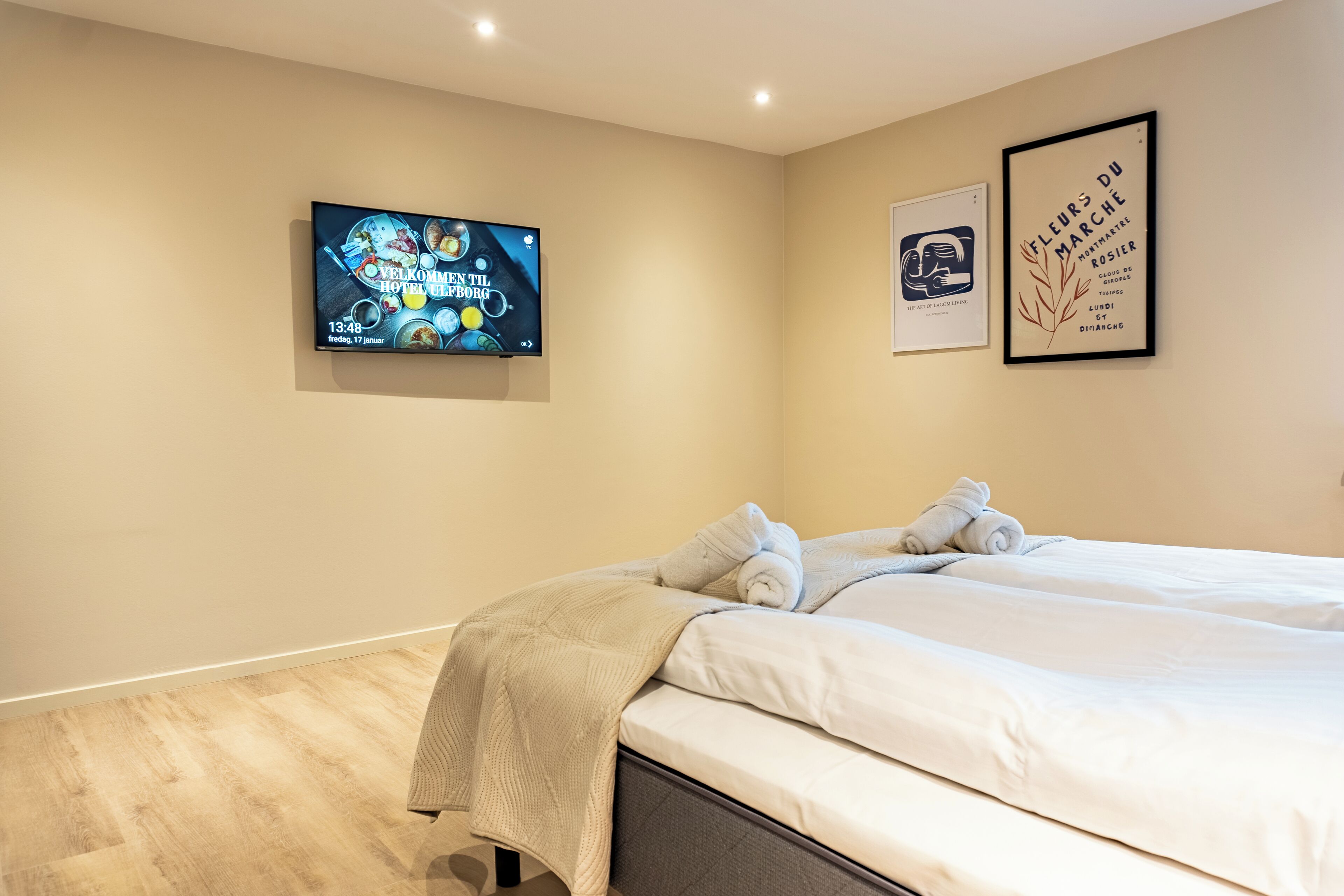 Una habitación de hotel moderna con una cama grande, un televisor de pantalla plana montado en la pared y dos cuadros enmarcados.