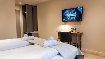 A hotel room with two beds, a TV mounted on the wall, a desk with a chair, and a small table with a kettle and cups.