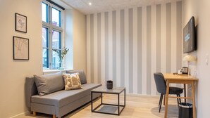 A modern living room with a grey sofa, a small coffee table, a wooden desk, and a TV mounted on the wall. - Hotel Ulfborg (Ulfborg)
