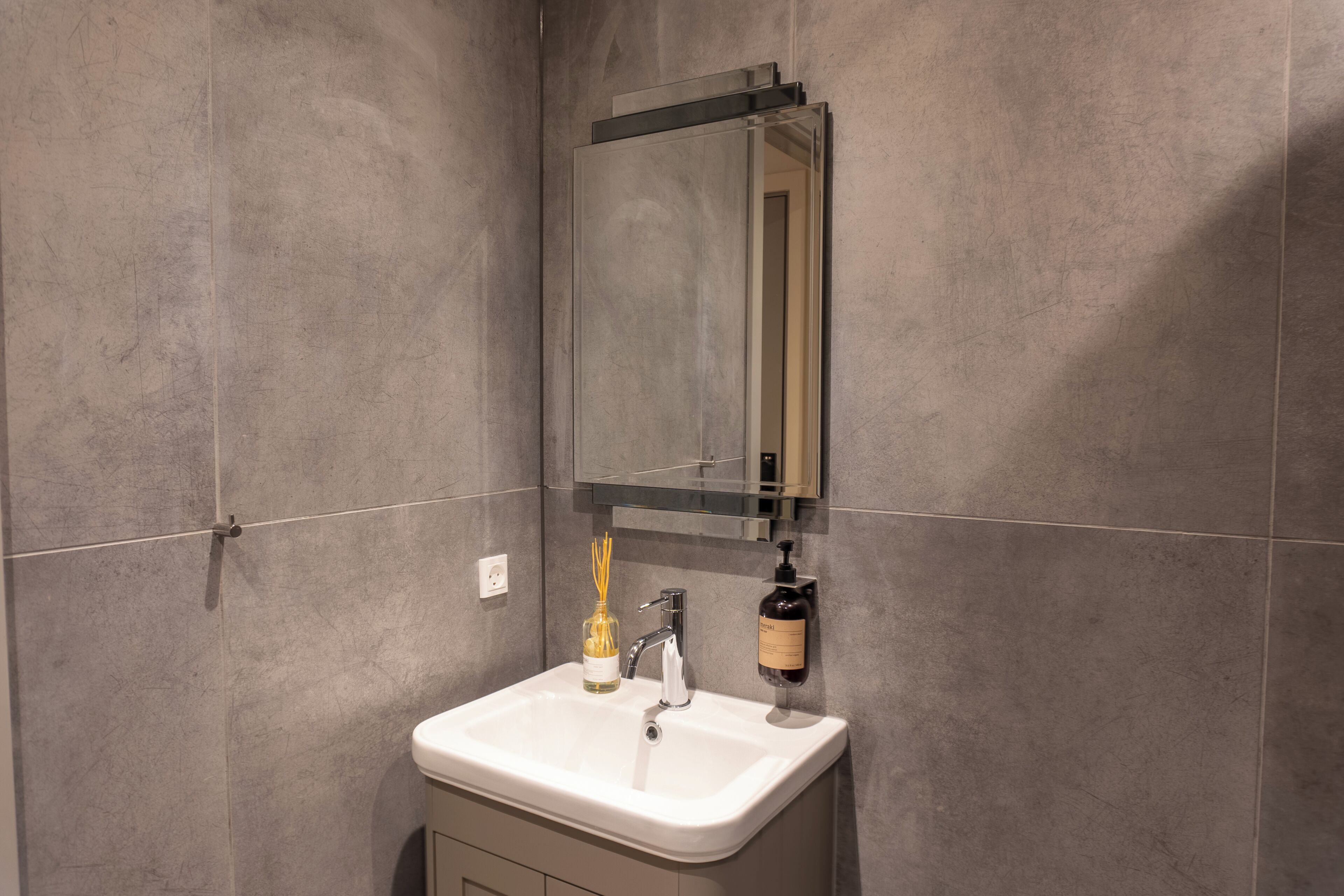 Un bagno con un lavandino bianco, uno specchio e un erogatore di sapone.
