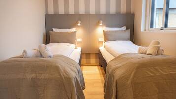 Habitación de hotel con dos camas, cada una con cabecera, lámparas de noche y una ventana con cortinas.