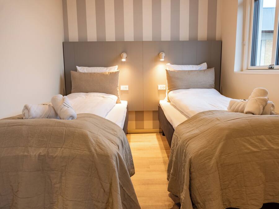 Habitación de hotel con dos camas, cada una con cabecera, lámparas de noche y una ventana con cortinas.