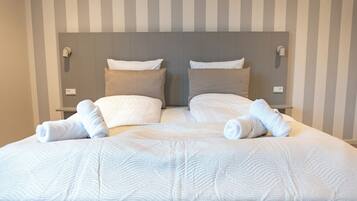 A double bed with white bedding and two pillows, a striped wall, and a headboard with light switches.