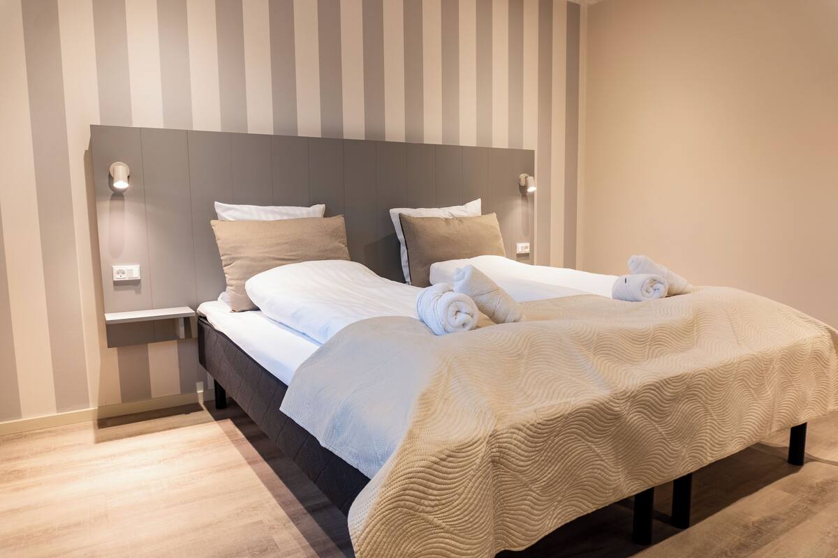 Ein modernes Hotelzimmer mit einem großen Bett, zwei Nachttischen und einem Kopfteil mit integrierter Beleuchtung.