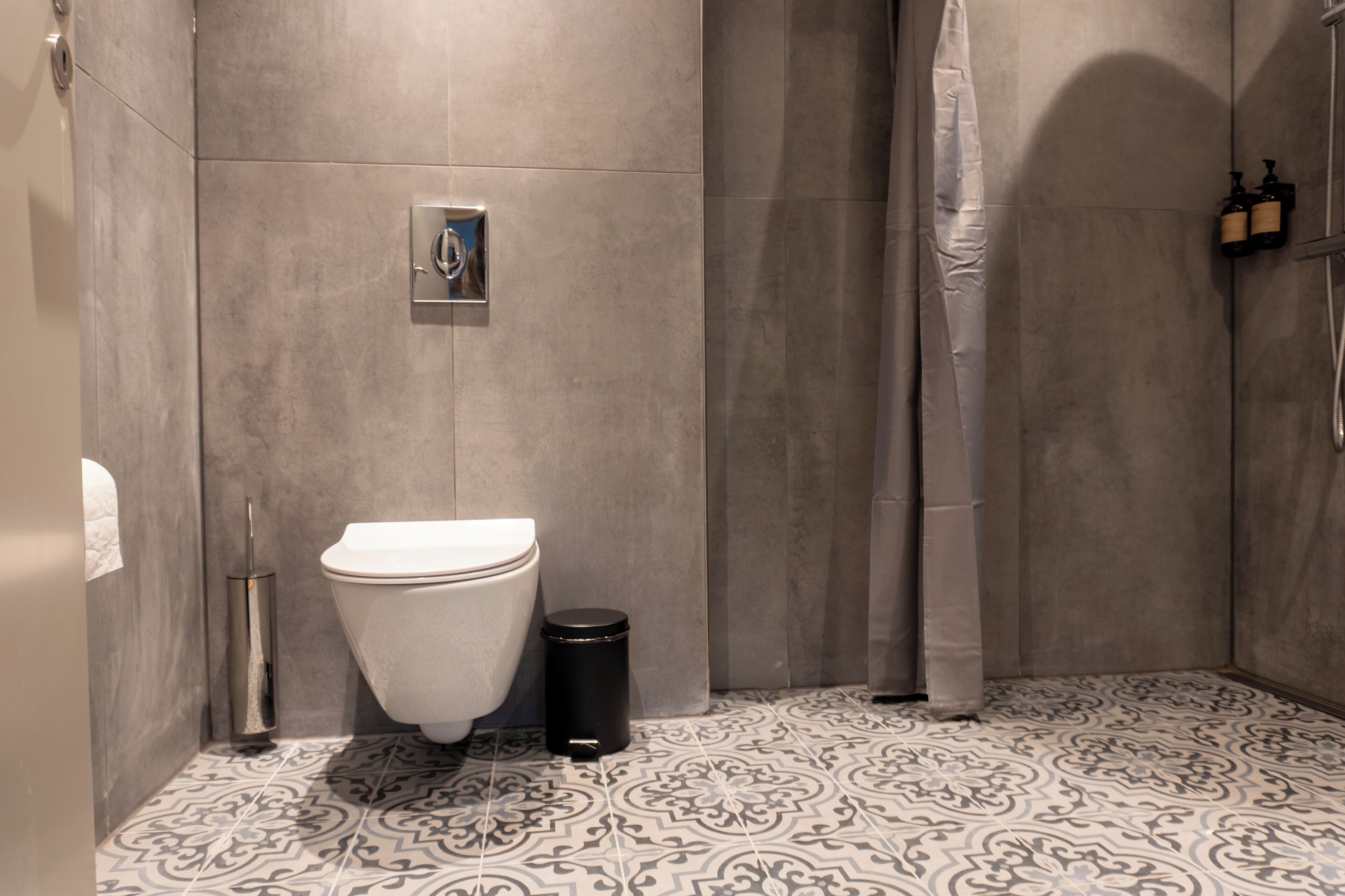 A bathroom with a toilet, a trash bin, a shower curtain, and a patterned floor.