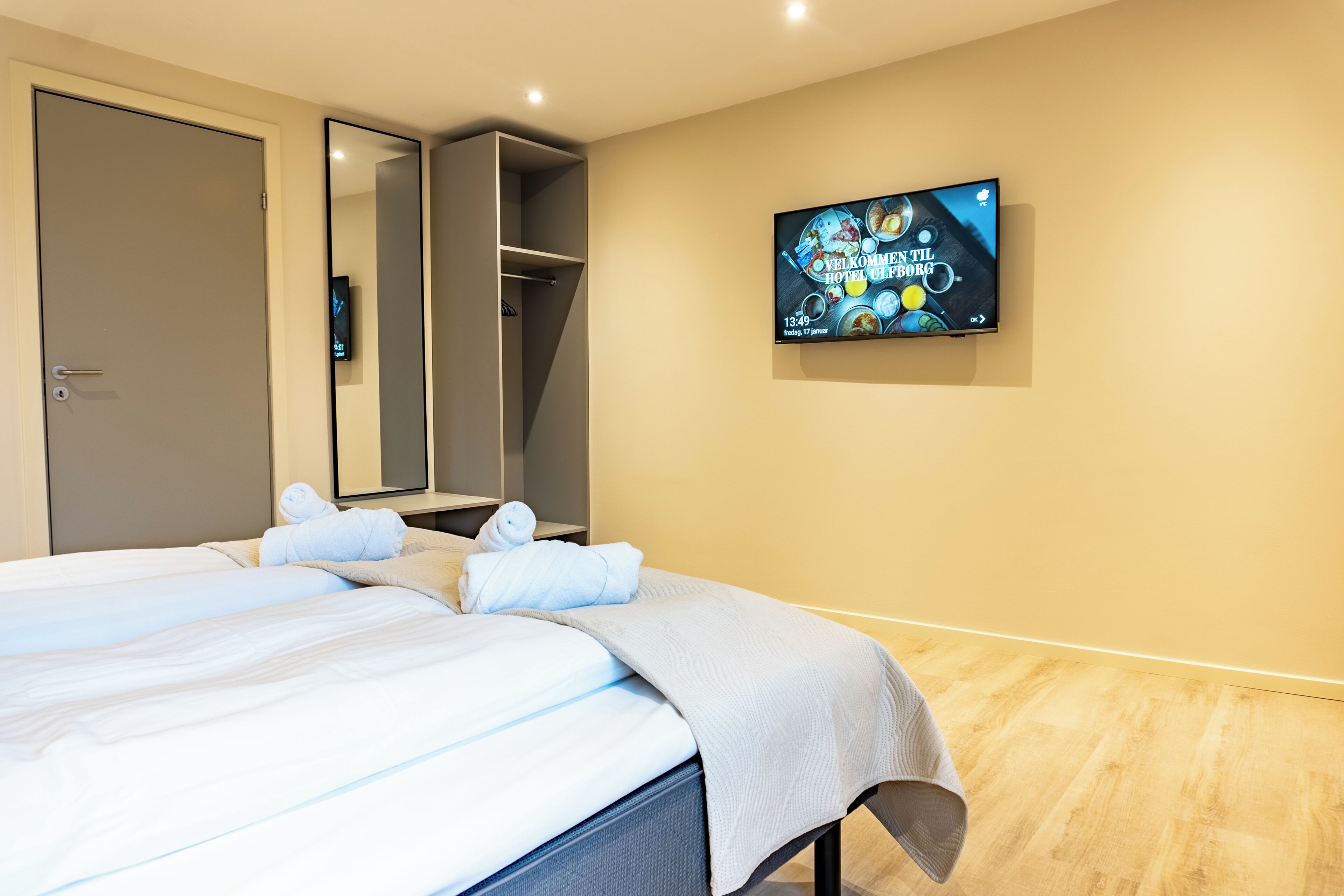 A hotel room with a bed, a TV mounted on the wall, and a wardrobe.