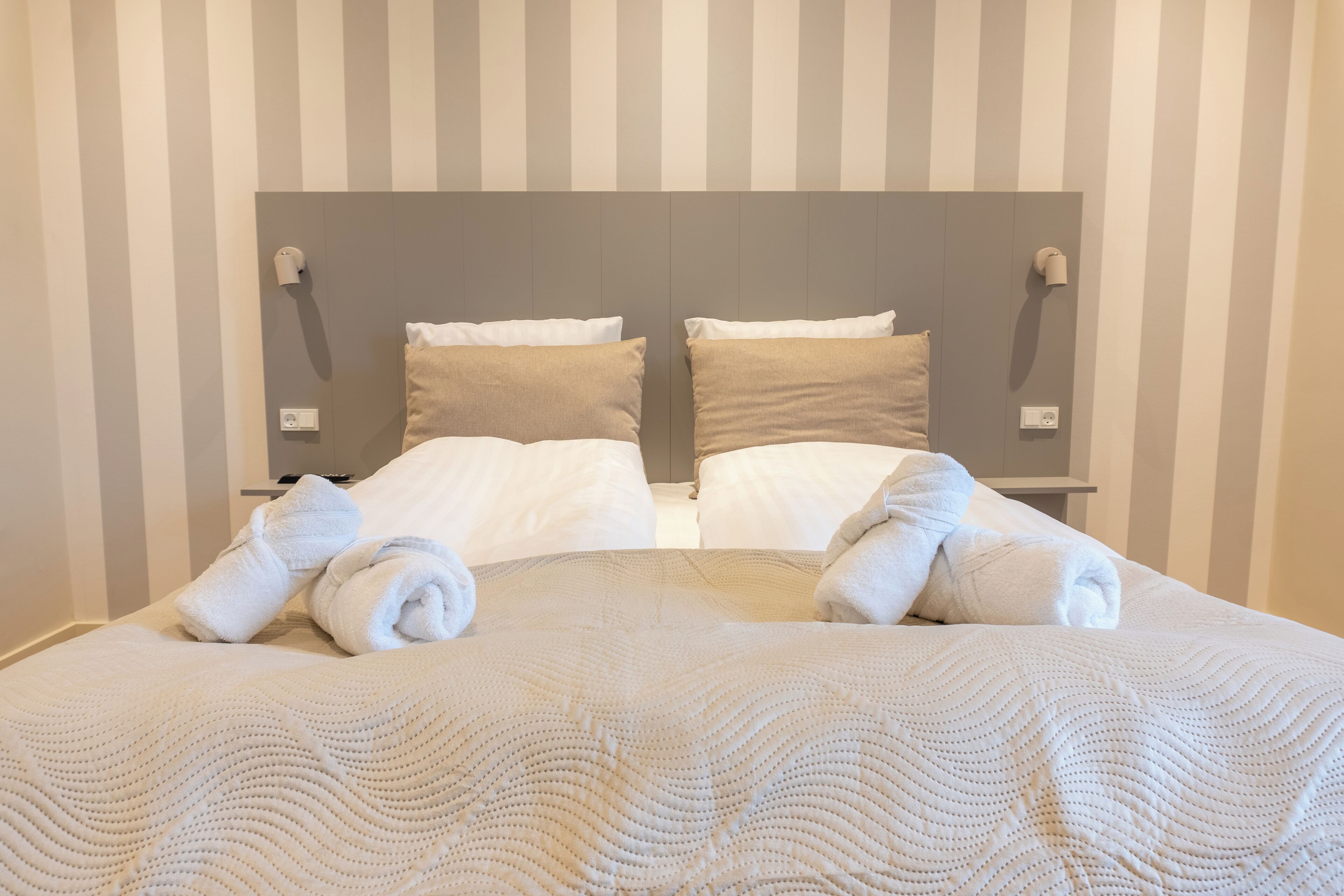 A neatly made bed with white linens and a textured blanket, positioned against a striped wall with two bedside lamps.