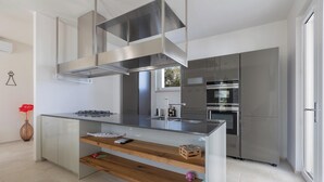 A modern kitchen with a central island, stainless steel appliances, and a large window. - Borgo Morgicchio by Perle di Puglia (Carovigno)