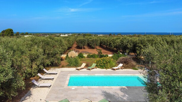 A swimming pool with lounge chairs, surrounded by greenery and a view of the sea. - Borgo Morgicchio by Perle di Puglia (Carovigno)