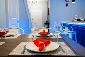 A dining table set with white plates, red napkins, and silverware, with a blue-lit bar area in the background.