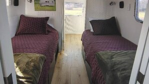 En smal korridor med två sängar på var sin sida, ett fönster i ena änden och en dörr som leder ut till ett utomhusområde.