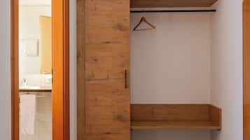 A hallway with a wooden wardrobe, a hanging coat rack, and a colorful abstract art piece on top.