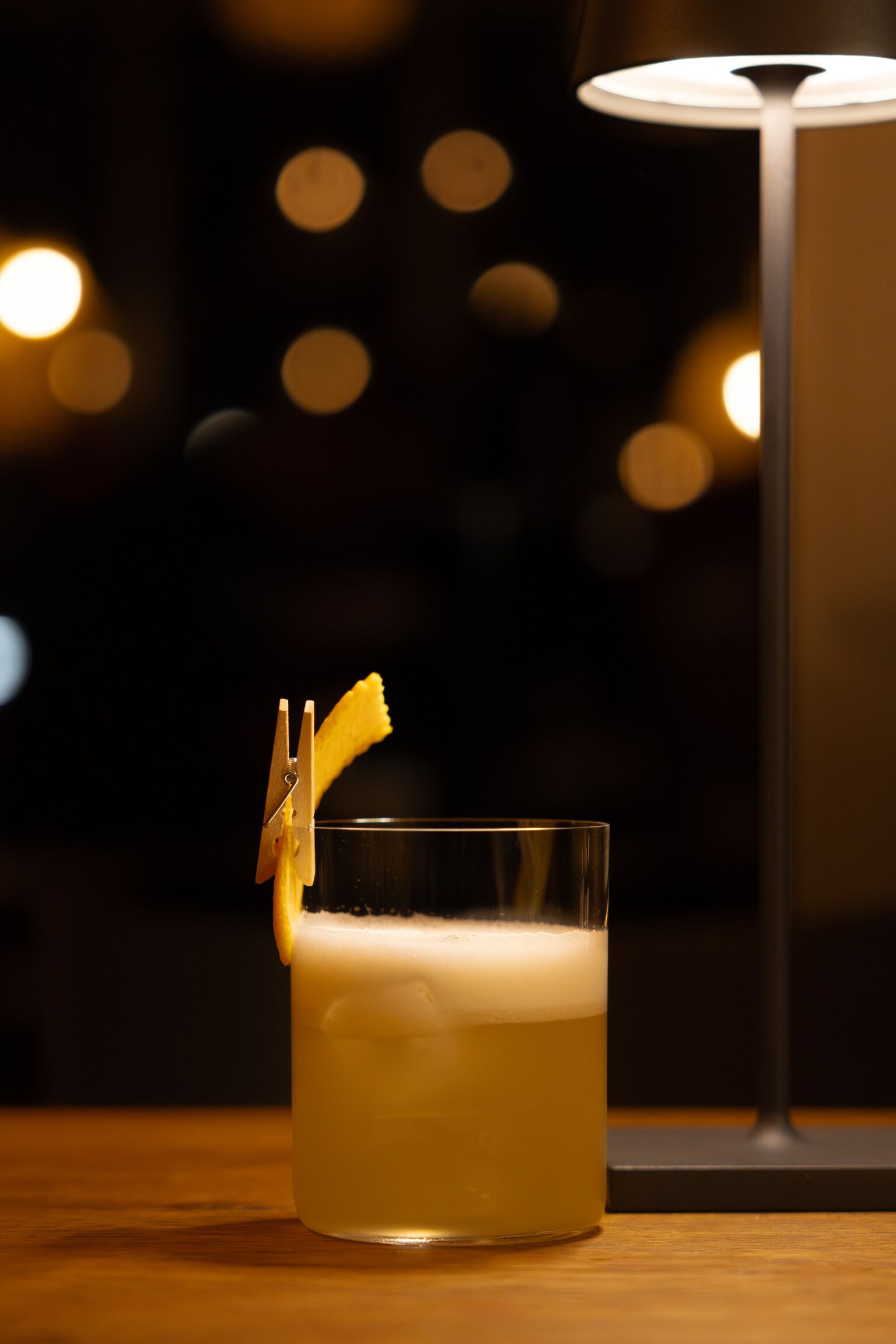 A glass of beer with a lemon peel garnish on a wooden table.