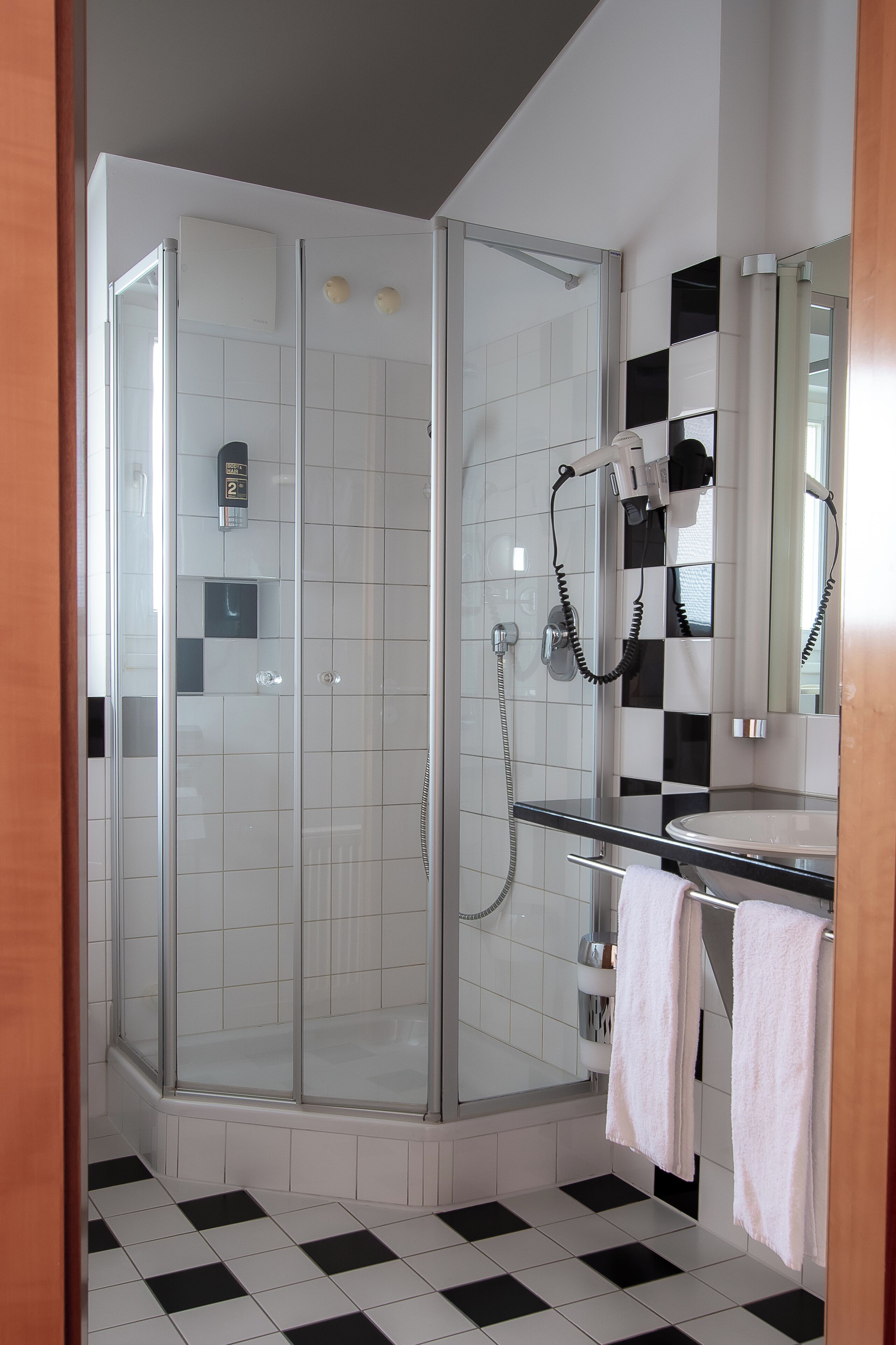 Ein modernes Badezimmer mit einer Duschkabine aus Glas, einem weißen Waschbecken und einem schwarz-weißen Schachbrettboden.