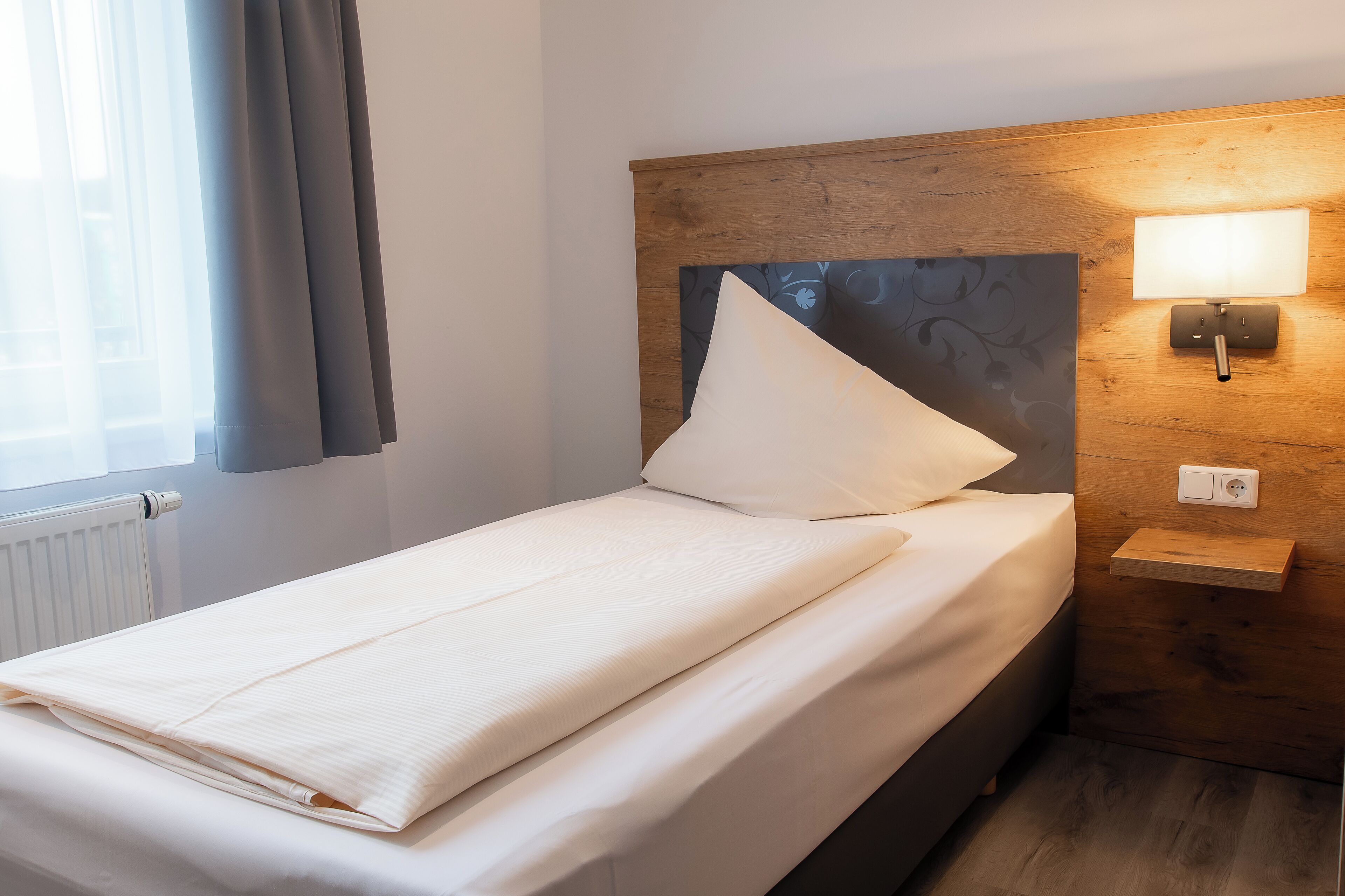 A neatly made bed with a pillow, a bedside table with a lamp, and a wooden headboard.