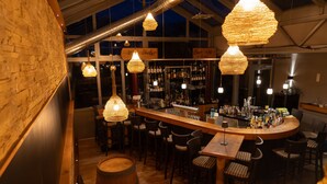 Una zona de bar con mobiliario de madera, lámparas colgantes y una barra con botellas.