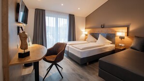Una habitación de hotel con una cama, un escritorio con silla, un televisor montado en la pared y una ventana con cortinas.