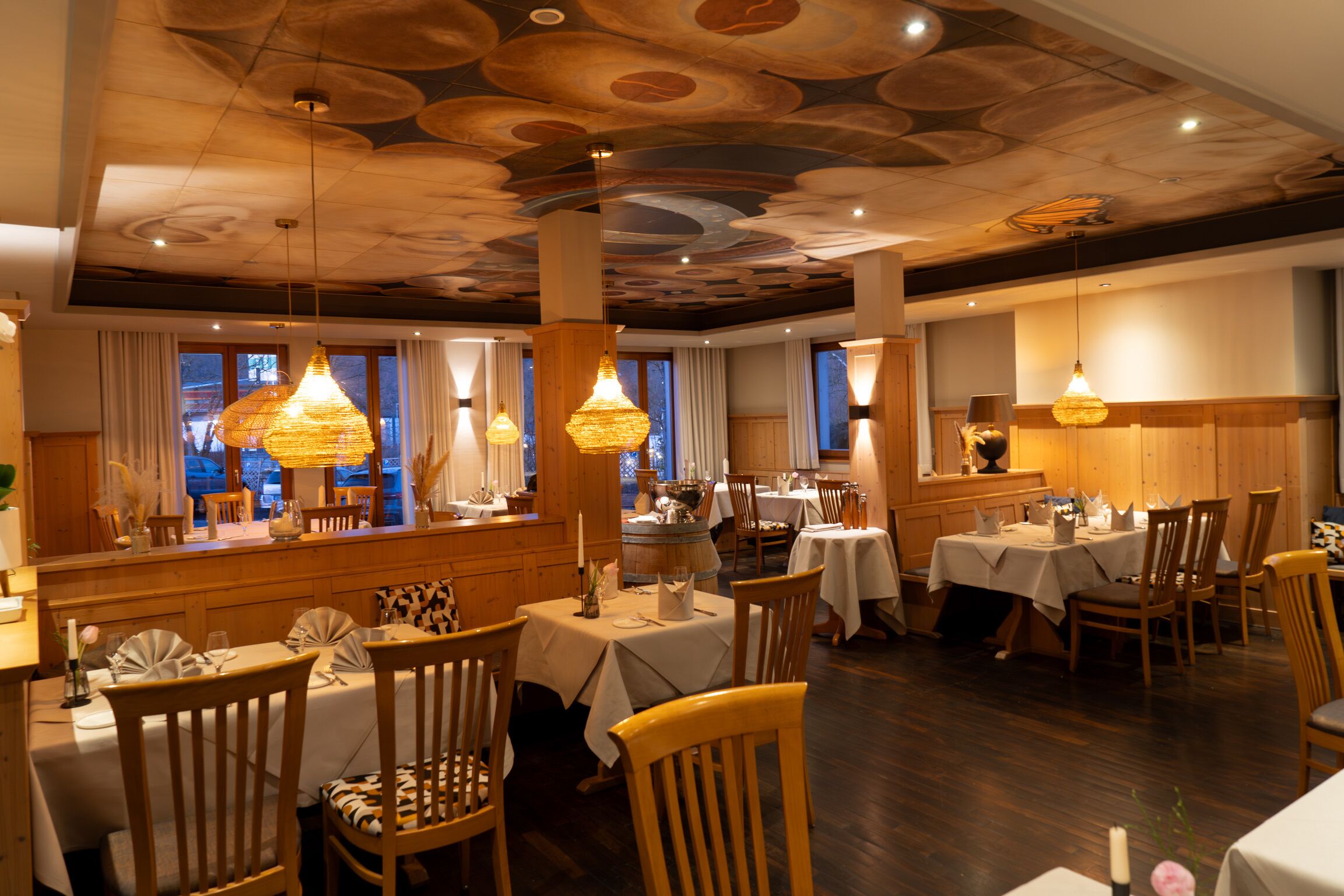 Un restaurante con muebles de madera, manteles blancos y lámparas colgantes.