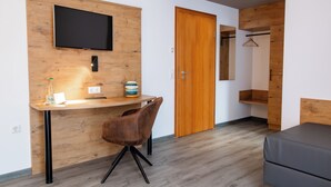 Una habitación moderna con un escritorio de madera, un televisor de pantalla plana, una silla marrón, un sofá gris y un armario de madera con espejo.