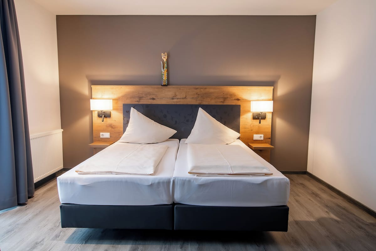 A double bed with white linens, two bedside tables with lamps, a wooden headboard, and a decorative item above the headboard.