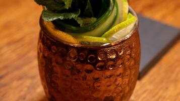 A copper mug with a textured pattern, containing a beverage garnished with mint leaves, cucumber slices, and a lemon wedge, with a straw.