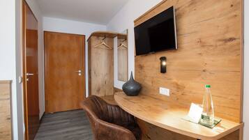 A hotel room with a wooden desk, a brown leather chair, a flat-screen TV mounted on the wall, and a wooden wardrobe.