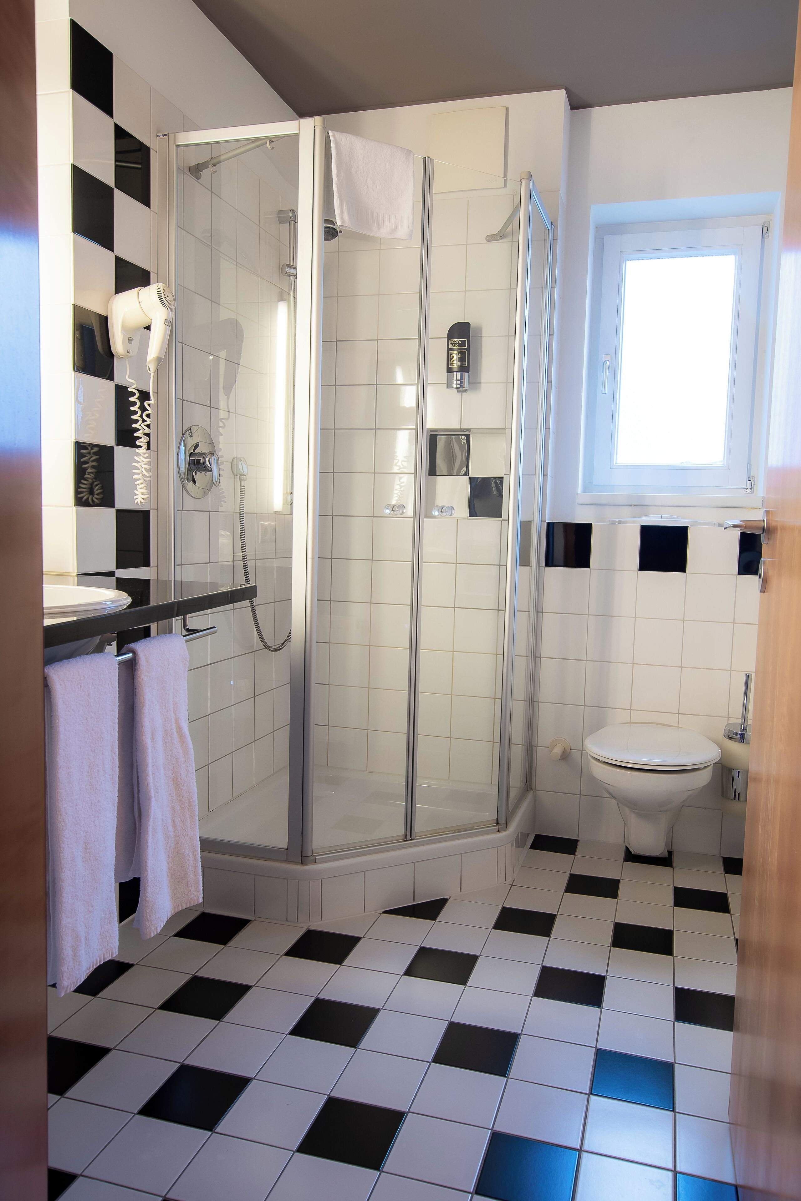 Un baño con ducha envuelta en vidrio, inodoro y lavamanos con toallero.