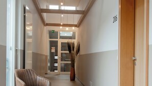 Un pasillo con una puerta de madera con la leyenda '206', una silla y un jarrón grande con plantas secas.