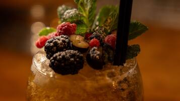 A cocktail with ice, blackberries, raspberries, and mint leaves, garnished with a black straw.