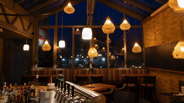 Un restaurante con techo alto, ventanas amplias y lámparas colgantes.