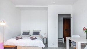 Un dormitorio moderno con una cama, mesita de noche, lámpara y una pequeña mesa con sillas.