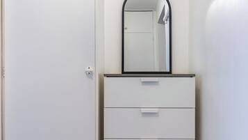 A white wardrobe with a mirror, a bench, and a small table.