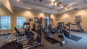 Une salle de sport équipée de divers appareils d’exercice, dotée de grandes fenêtres et de ventilateurs de plafond.