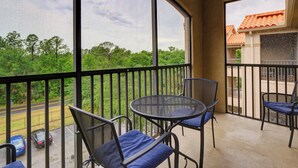 Un balcon donnant sur une route et sur un espace verdoyant, avec une table ronde et des chaises.