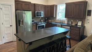A kitchen with wooden cabinets, stainless steel appliances, a central island with stools, and a window providing natural light.