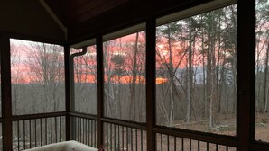 A covered porch with a view of a forest and a sunset.